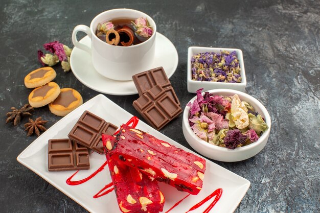 Foto lateral de un plato de chocolate con una taza de té de hierbas y flores secas sobre suelo gris