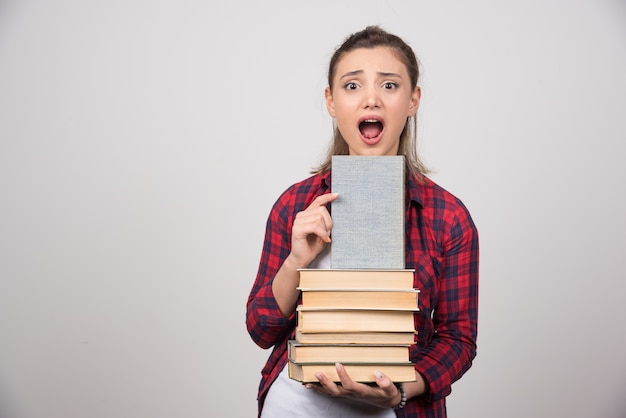 Foto de una linda joven estudiante sosteniendo una pila de libros.