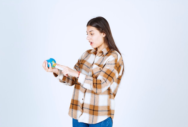 Foto de linda mujer joven mirando el pequeño globo en la pared blanca.