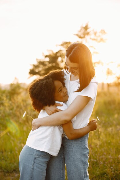 Foto de madre caucásica y su hija afroamericana abrazándose juntos en una puesta de sol. La chica tiene el pelo negro y rizado