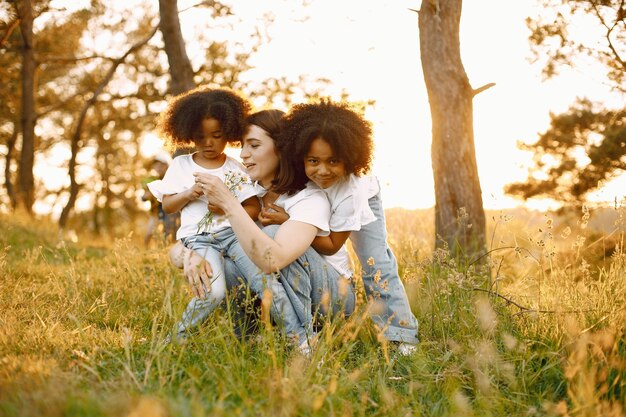 Foto de madre caucásica y sus dos hijas afroamericanas abrazándose juntos al aire libre. Las chicas tienen el pelo negro y rizado.