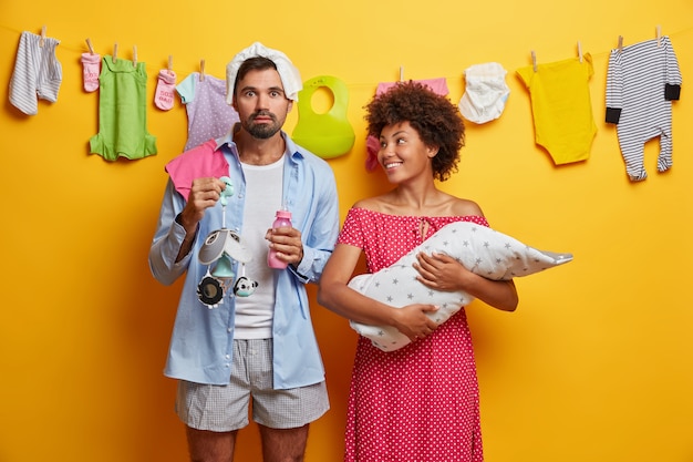 La foto de la madre feliz sostiene al bebé recién nacido y mira al esposo que ayuda con la lactancia infantil, sostiene el biberón móvil. Los padres jóvenes cuidan a un bebé pequeño. Familia, concepto de paternidad.