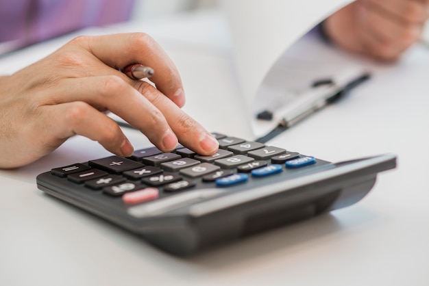 Foto de manos sosteniendo lápiz y presionando botones de calculadora sobre documentos