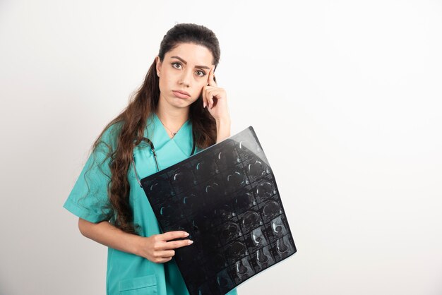 Foto de un médico joven sosteniendo una radiografía sobre una pared blanca.