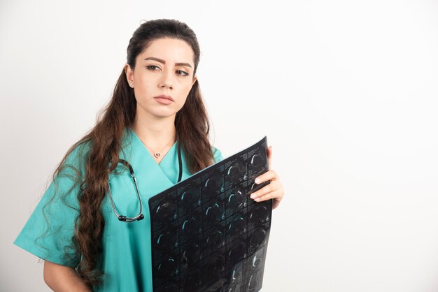 Foto de un médico joven sosteniendo una radiografía sobre una pared blanca.