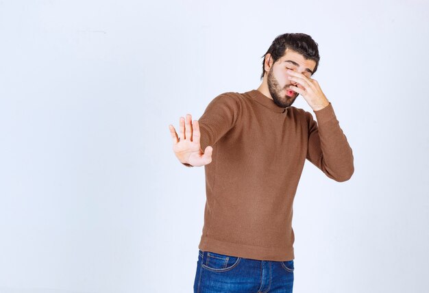 Foto de un modelo de hombre guapo joven que cubre su nariz sobre una pared blanca. Foto de alta calidad