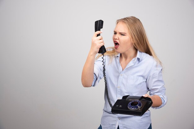 Foto de un modelo de mujer enojada de pie y gritando en el teléfono viejo negro