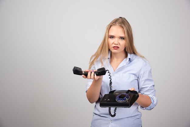 Foto de un modelo de mujer enojada de pie y sosteniendo un auricular viejo negro