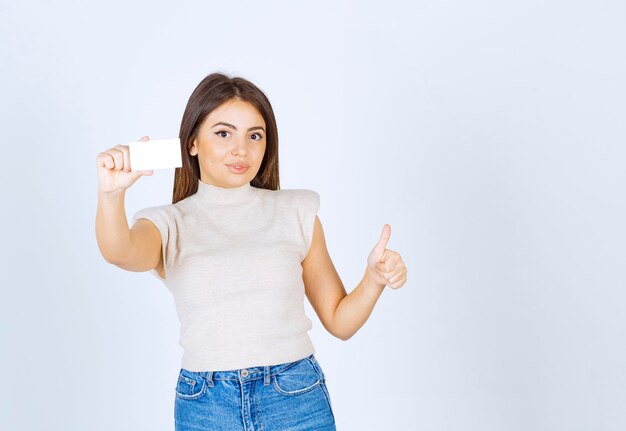 Foto de modelo de mujer hermosa joven sosteniendo una tarjeta y mostrando un pulgar hacia arriba.