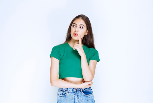 Foto de un modelo de niña pensativa de pie y posando contra la pared blanca.