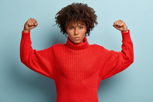 Foto de mujer afroamericana furiosa y enojada que mantiene los brazos en alto, aprieta los puños y muestra los músculos