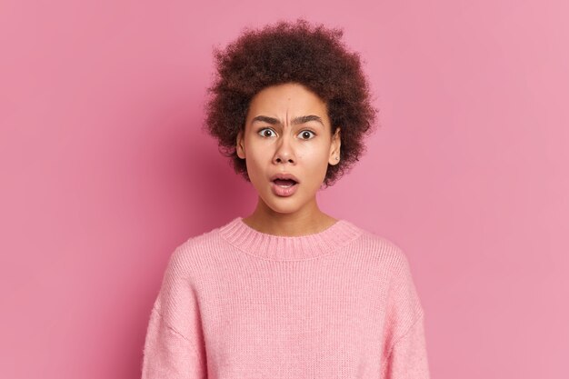 Foto de mujer afroamericana sorprendida y perpleja mira a la cámara con gran asombro e incredulidad mantiene la boca abierta