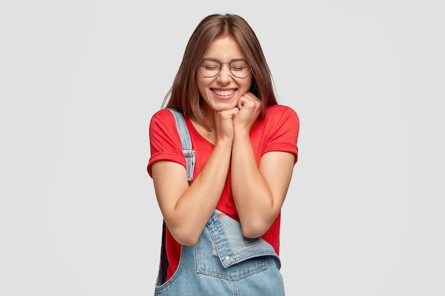 Foto de mujer atractiva tiene placer, estar impresionado por algo positivo, mantiene las manos juntas