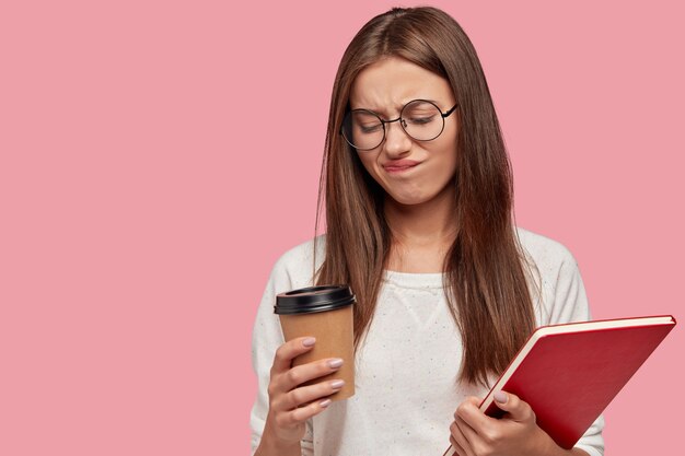 Foto de mujer bonita de cabello oscuro frunce el ceño con disgusto sostiene café para llevar