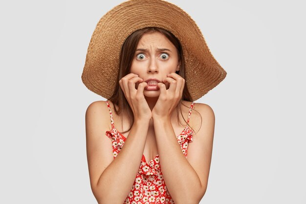 Foto de mujer caucásica asustada asustada con ojos verdes, aprieta los dientes por miedo, mantiene las manos cerca de la boca