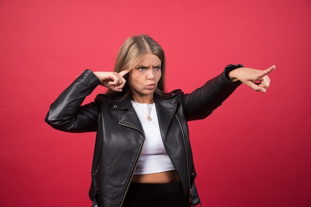 Foto de mujer con chaqueta de cuero apuntando hacia afuera y dando dirección