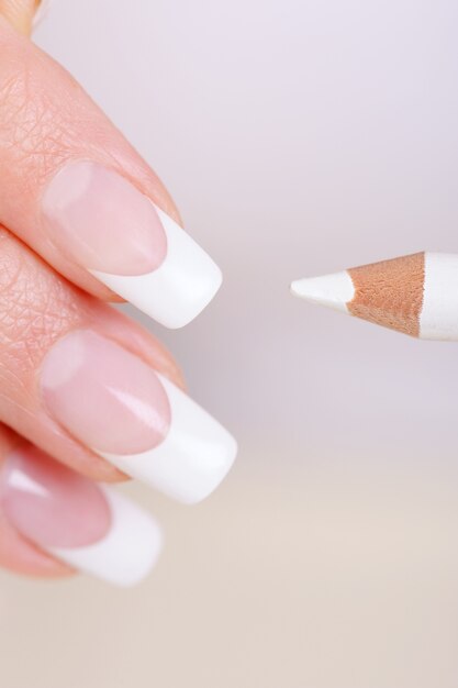 Foto de una mujer dedos con un lápiz blanco de manicura