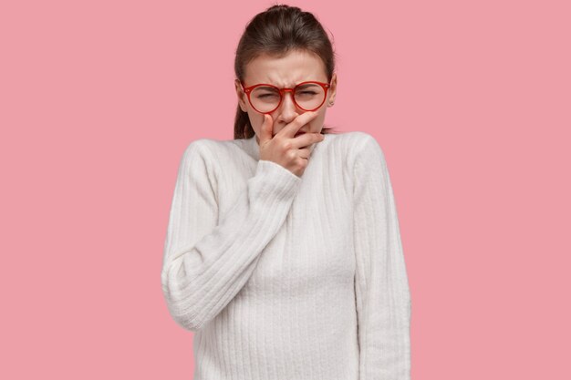 La foto de una mujer desesperada llora desesperada, tiene un fracaso en la vida, se cubre la boca, expresa emociones negativas, usa un suéter informal, modelos sobre la pared rosa del estudio. Personas