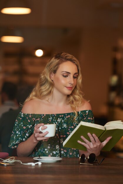 Foto de mujer despreocupada leyendo un libro en una cafetería