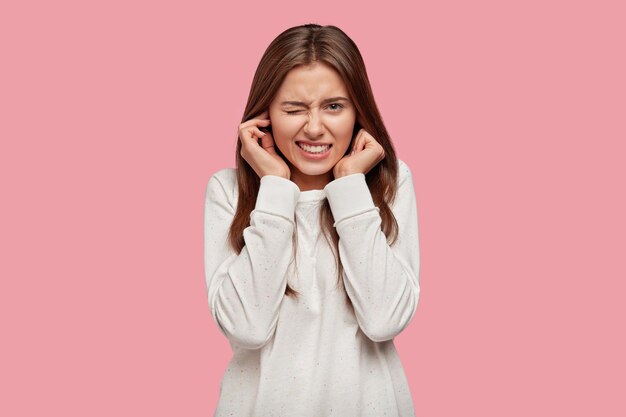 Foto de mujer disgustada que se tapa los oídos con descontento, no quiere escuchar sonidos o ruidos molestos