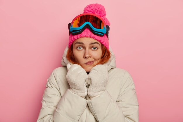 Foto de mujer encantadora viajera frunce los labios, se calienta con ropa de abrigo cómoda durante el invierno, usa pasamontañas