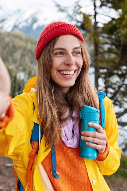 La foto de una mujer europea feliz tiene una amplia sonrisa, muestra unos dientes blancos perfectos, hace una foto de sí misma, toma un café