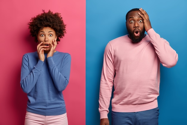 Foto de una mujer y un hombre de piel oscura abrumados y asustados que miran juntos una película de terror, visten ropa azul y rosa, tiemblan de miedo