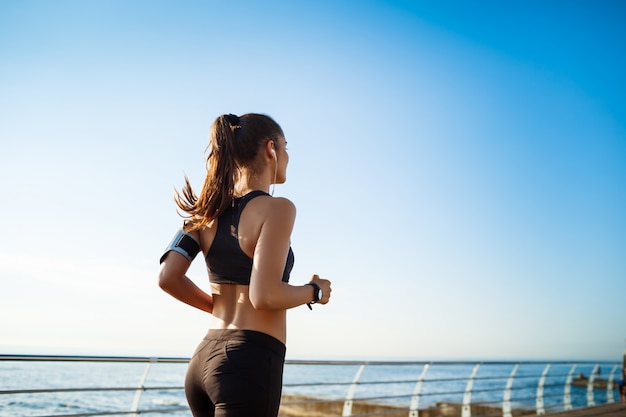 Foto de mujer joven atractiva fitness trotar con mar en la pared
