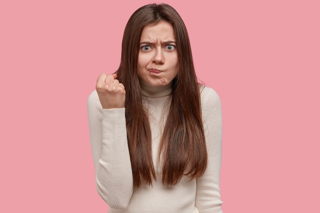 Foto gratuita foto de mujer joven disgustada frunce el ceño, muestra el puño, se siente insatisfecha, advierte sobre algo