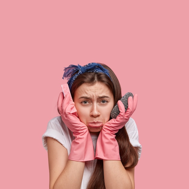 Foto de mujer joven disgustada que se abrocha el labio inferior, tiene el pelo largo y oscuro, se siente con exceso de trabajo después de hacer la limpieza de primavera en la casa