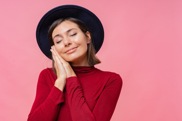 Foto de mujer joven europea satisfecha con una amplia sonrisa agradable, mantiene los ojos cerrados, sueña con algo agradable, vestida con un jersey informal, aislado.