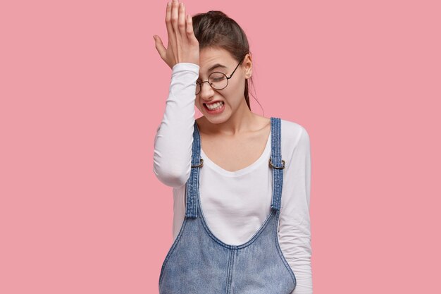 Foto de mujer joven insatisfecha lamenta haber hecho mal, mantiene la mano en la frente, aprieta los dientes