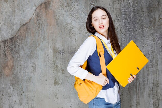 Foto de mujer joven con mochila amarilla de pie sobre la pared. foto de alta calidad