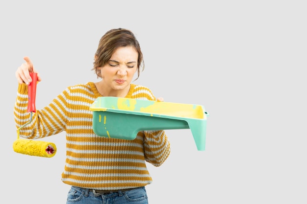 Foto de mujer joven de pie y sosteniendo un rodillo de pintura en la mano. Foto de alta calidad