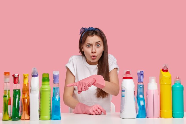 Foto de mujer joven sorprendida con expresión terrible, apunta a botellas de detergente, sorprendida con su maravilloso efecto