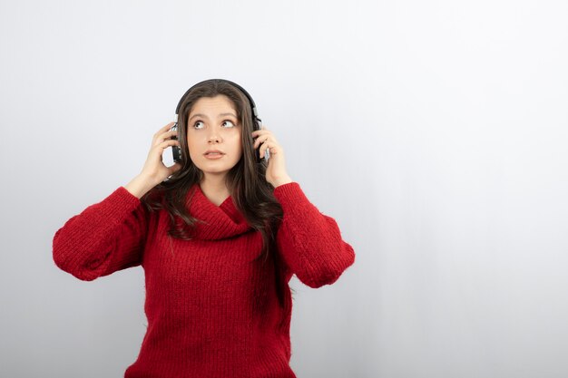 Foto de una mujer joven en suéter rojo con auriculares.