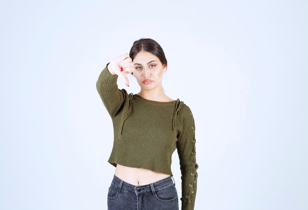 Foto de una mujer joven triste de pie y mostrando el pulgar hacia abajo.