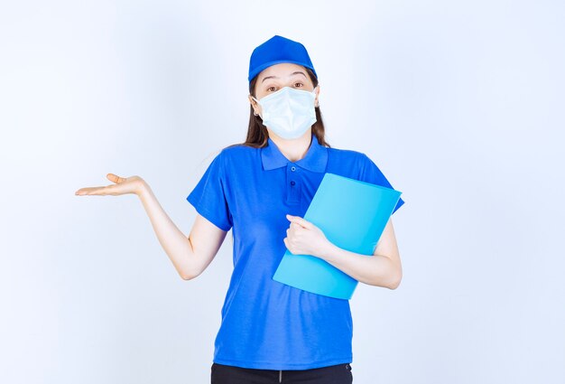 Foto de mujer joven en uniforme con máscara médica y carpeta de retención.