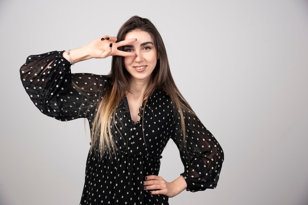 Foto de mujer joven con vestido sonriendo y mostrando el signo de la paz.