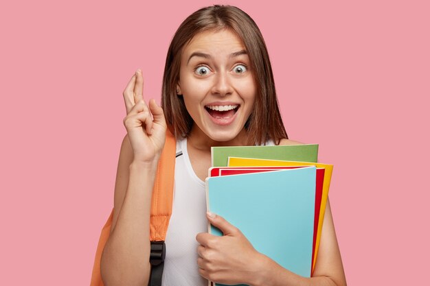 Foto de mujer morena alegre con mirada llena de alegría mantiene los dedos cruzados