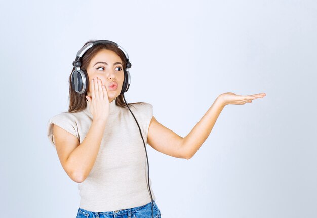 Foto de mujer muy agradable modelo escuchando música en auriculares y mostrando la mano.