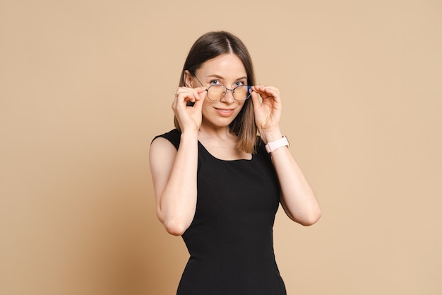 Foto de mujer de negocios caucásica joven feliz con gafas de pie sobre la pared beige