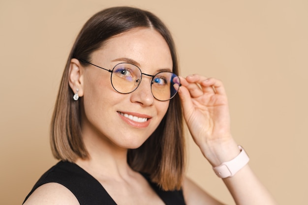 Foto gratuita foto de mujer de negocios caucásica joven feliz con gafas de pie sobre la pared beige