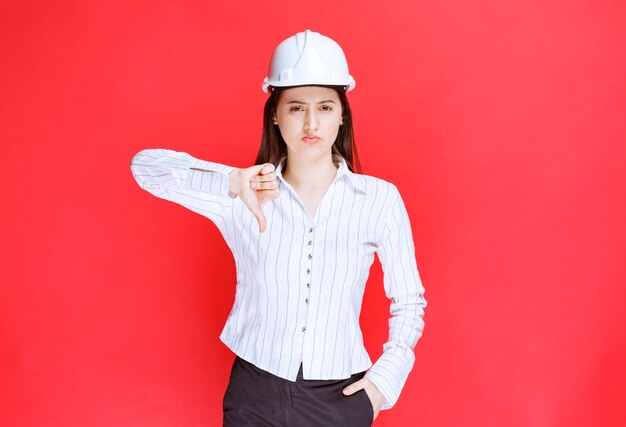 Foto de una mujer de negocios con sombrero de seguridad mostrando un pulgar hacia abajo.