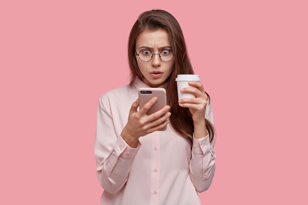 Foto de mujer de piel oscura sorprendida que mira con expresión de asombro en la pantalla del teléfono celular, tiene un problema, recibió noticias desagradables