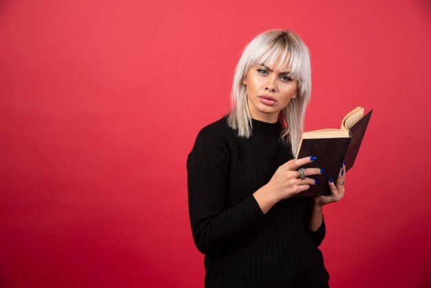 Foto de mujer rubia sosteniendo un libro y mirando a la cámara