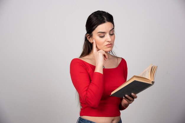 Foto de una mujer seria leyendo un libro y sosteniendo un lápiz.