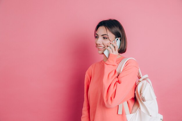 Foto de mujer sonriendo mientras habla por teléfono inteligente aislado sobre fondo de color rosa