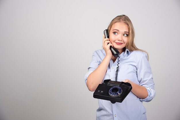 Foto de una mujer sonriente modelo de pie y sosteniendo un auricular viejo negro