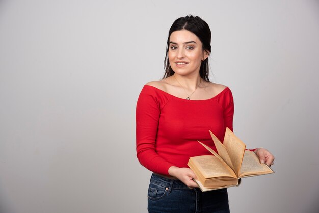 Foto de una mujer sonriente de pie y posando con un libro abierto.